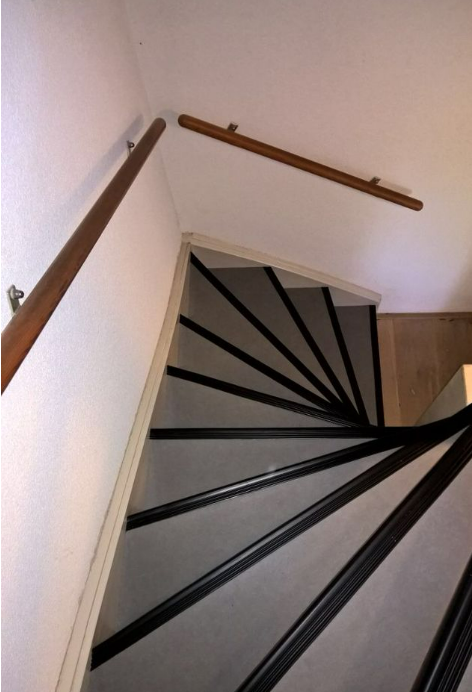 Cage d'escalier d'immeuble aux murs repeints en blanc, main courante bois et nez de marche noirs