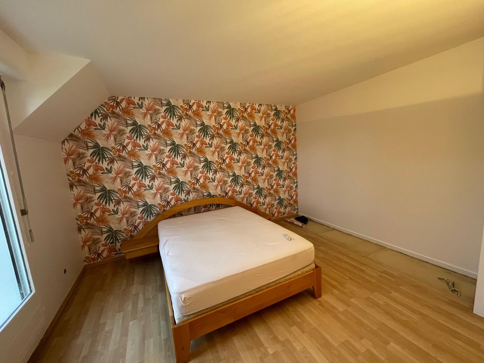 Chambre mansardée avec mur en papier peint tropical posé sous les combles d’un pavillon