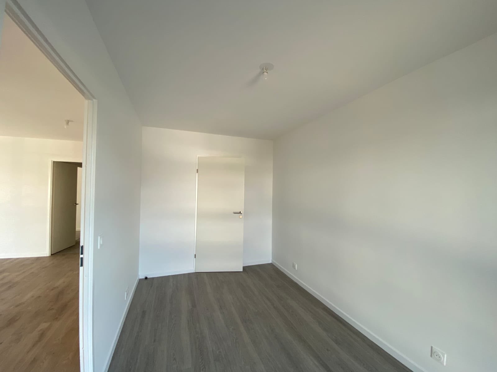 Chambre rénovée aux murs blancs et sol stratifié gris, prête à meubler