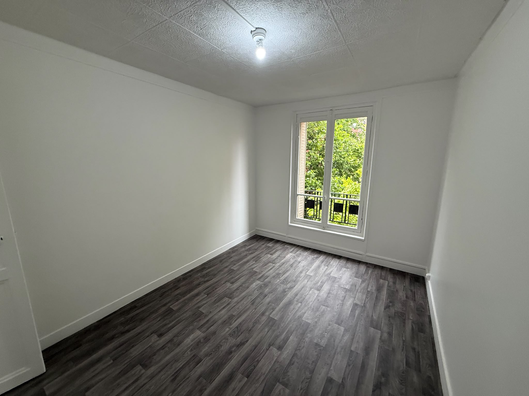 Chambre repeinte en blanc après remise en état locative, sol stratifié gris et fenêtre sur verdure