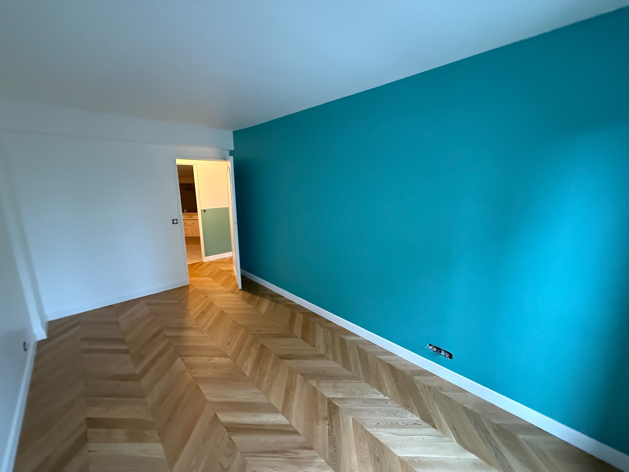 Mur d’accent repeint en bleu canard au-dessus d’un parquet à chevrons en chêne