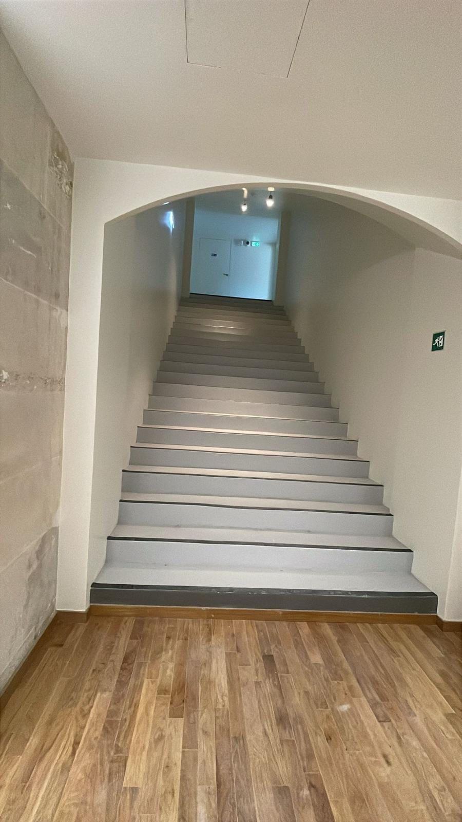 Cage d'escalier d'immeuble aux murs repeints en blanc, main courante bois et nez de marche noirs