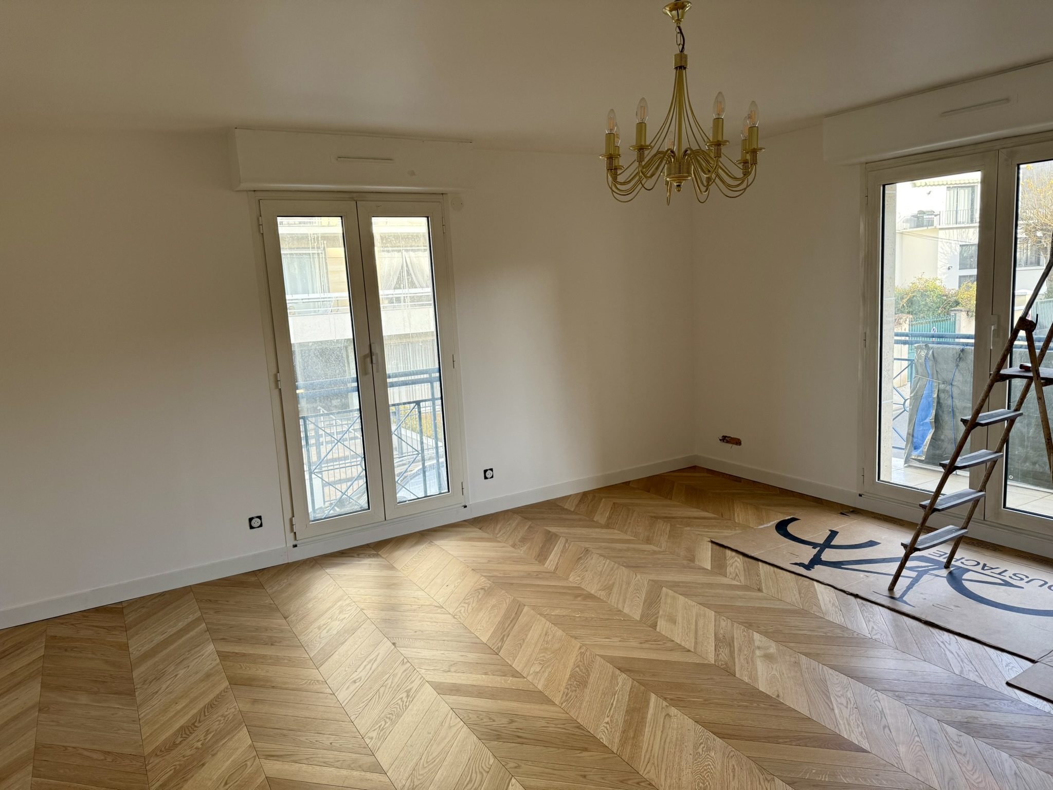 Sejour en cours de remise en peinture, murs blancs et parquet a chevrons protege